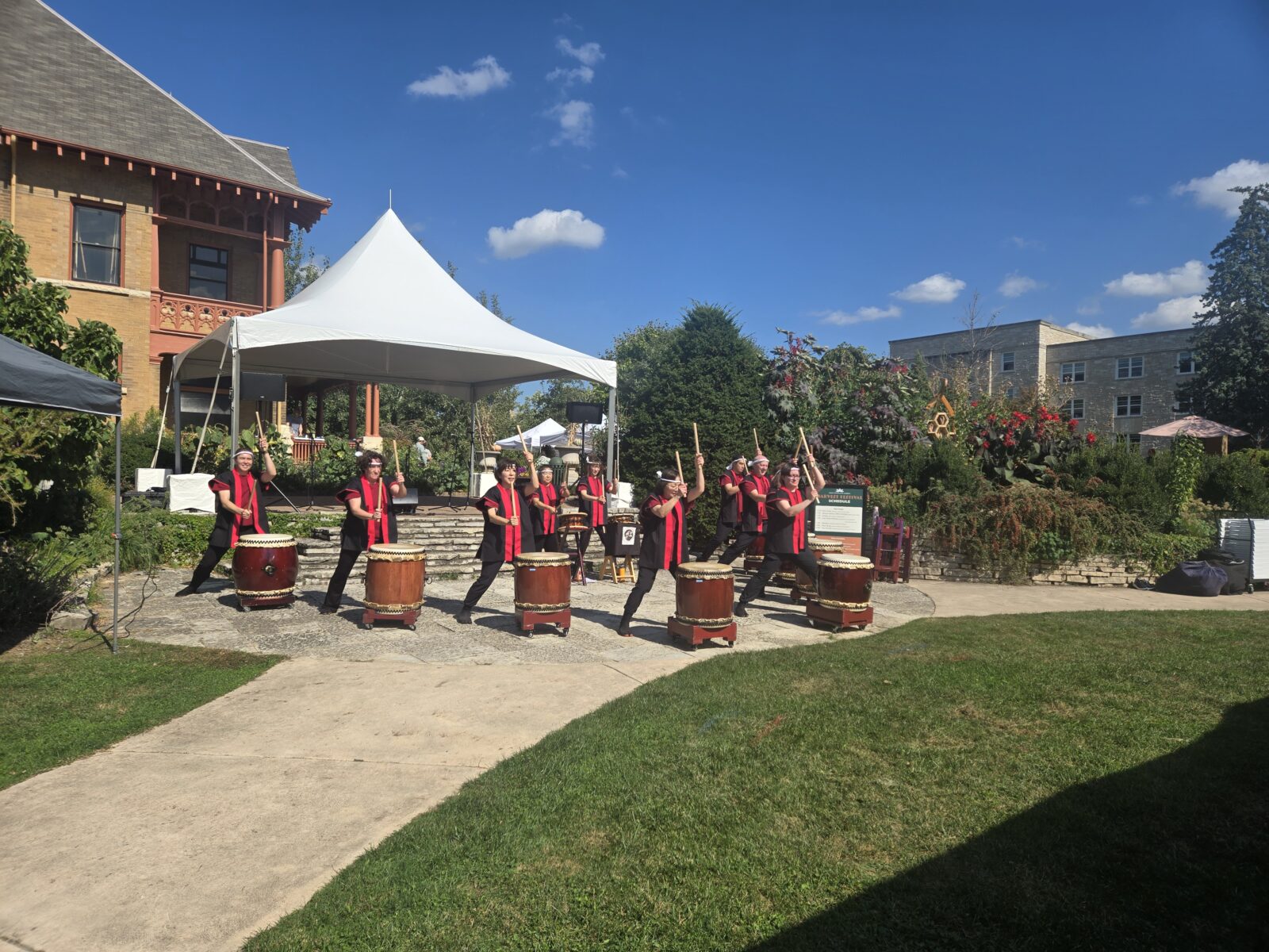 Taiko drumming group wearing red and black shirts each behind his or her own barrel-shaped drum.