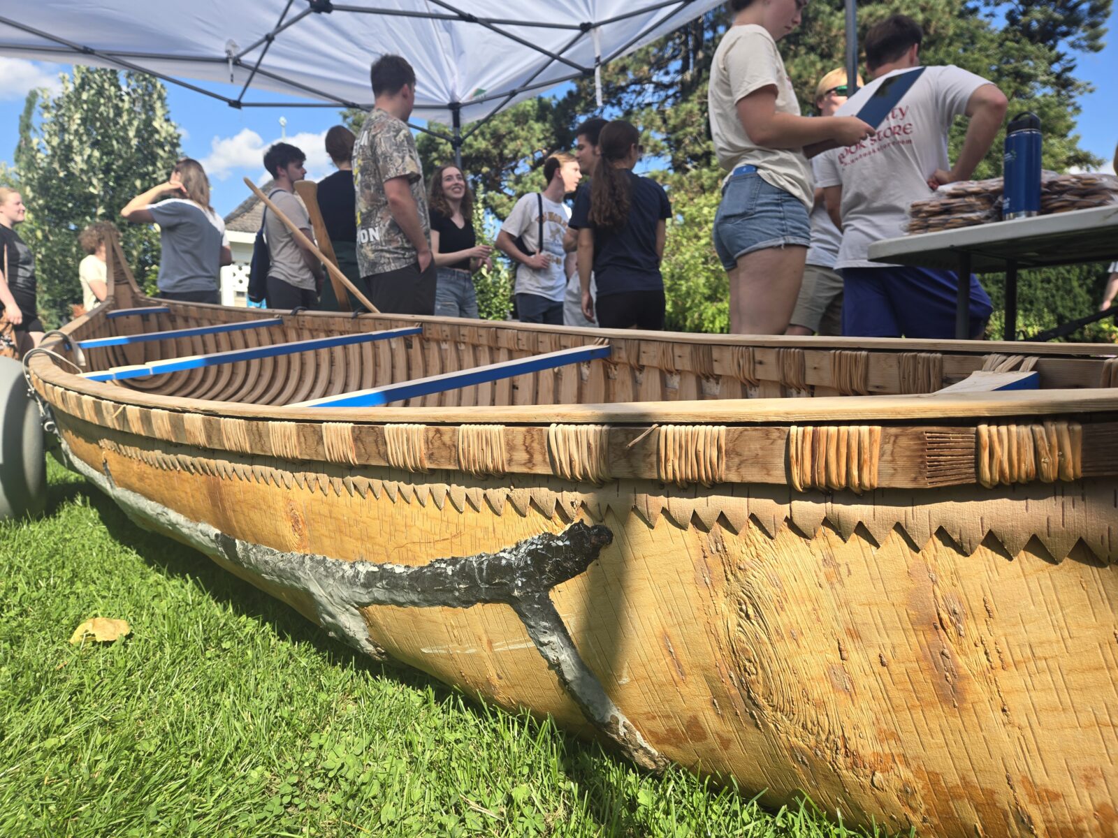 Birchbark canoe on grass with students milling around behind