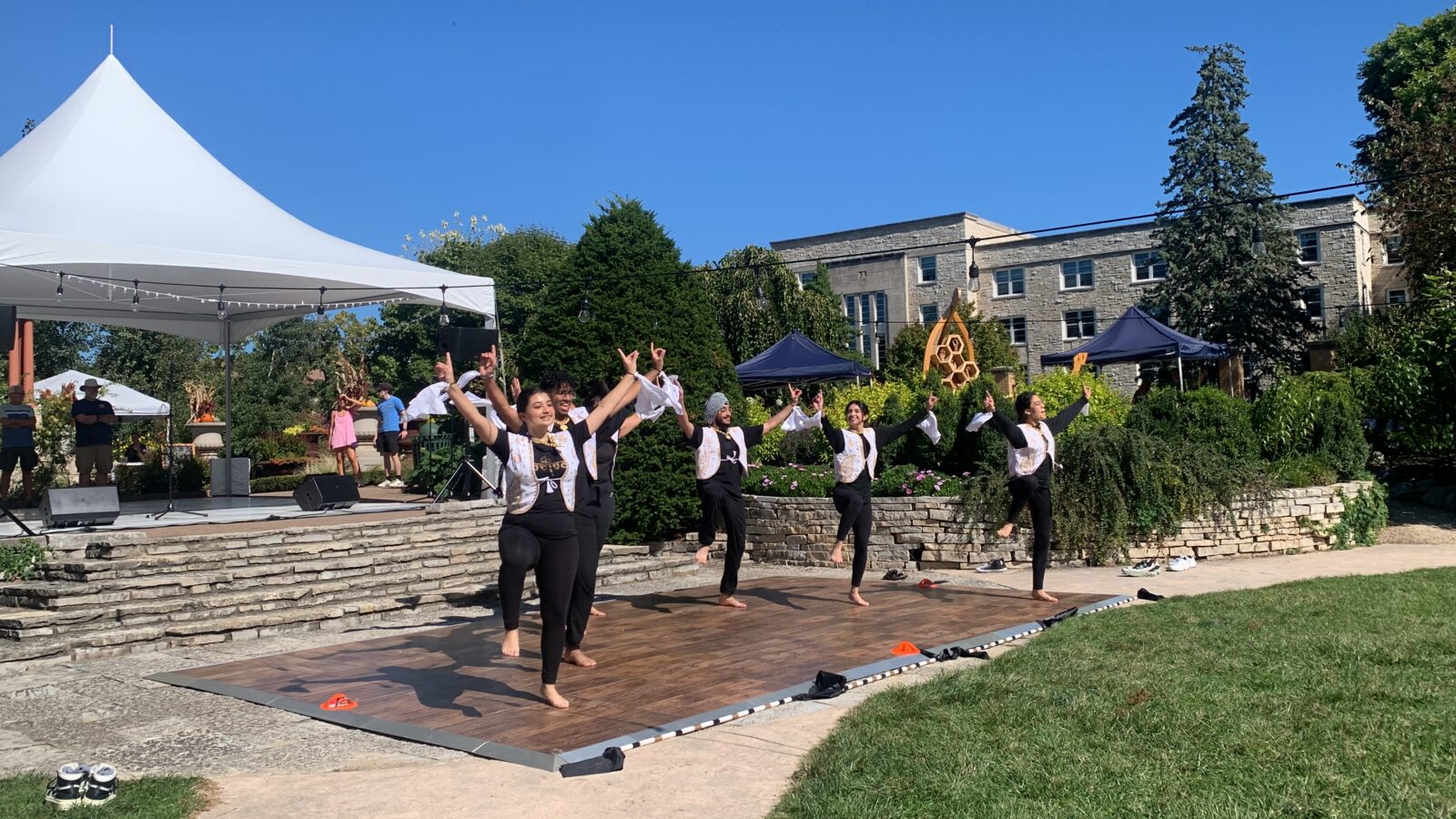 Students in black outfits with white vests performing Indian dances